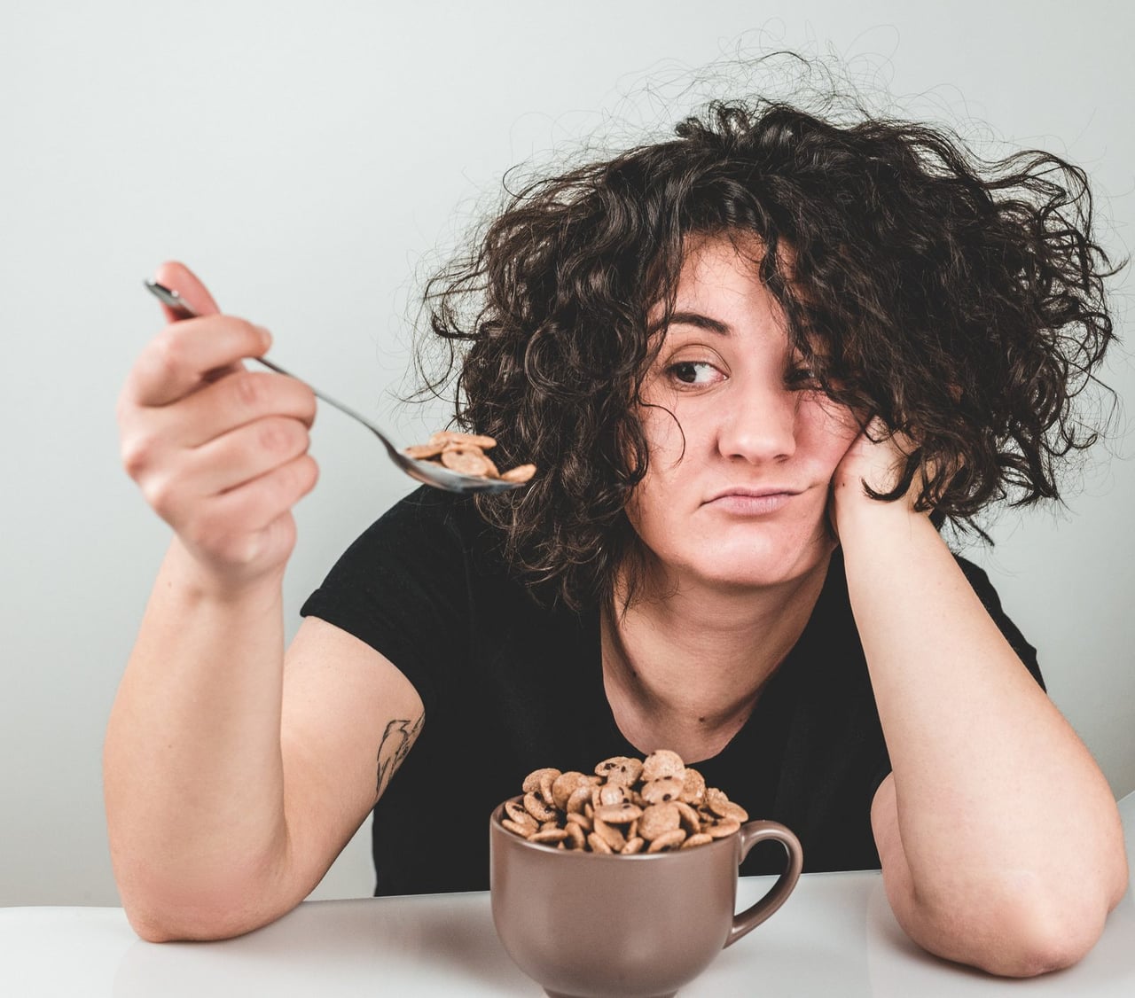 A woman at the table looking uncomfortable over a bowl of cereal